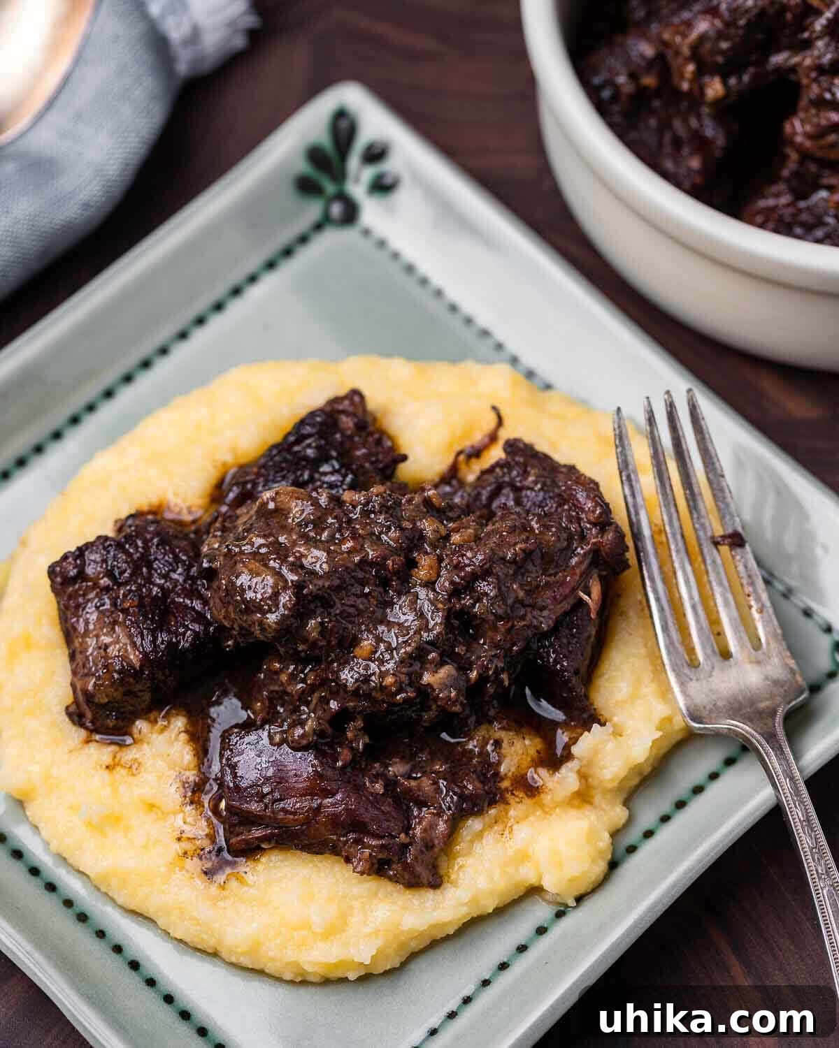 Tuscan Peppery Beef 7 A blue plate featuring a generous serving of Tuscan beef stew (Peposo) over a bed of creamy polenta, with a fork resting beside it.
