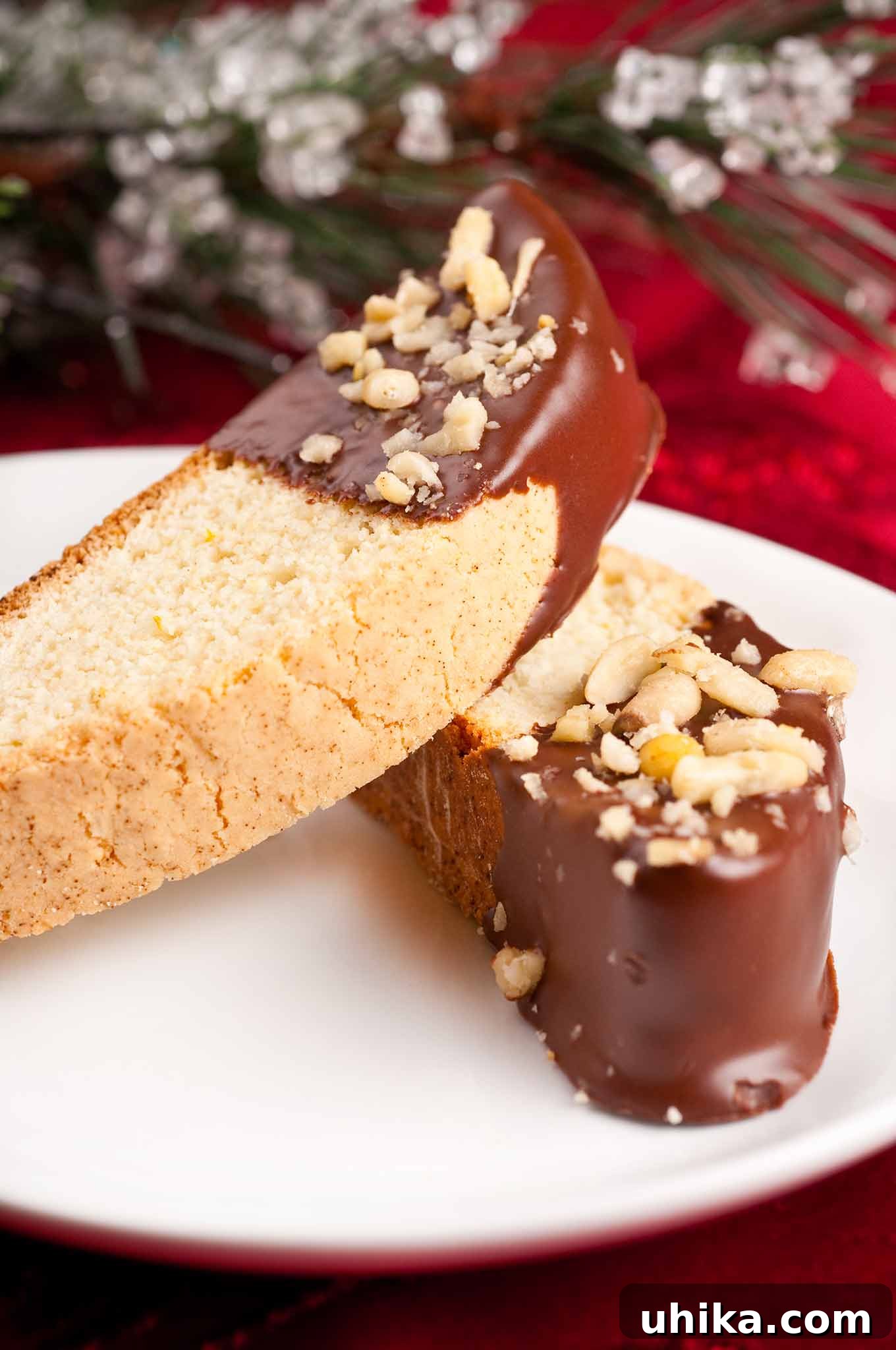 Zesty Butter Biscotti: A Double Treat 3 Two chocolate-dipped orange biscotti on a white serving plate, with subtle Christmas table decor in the soft-focus background.