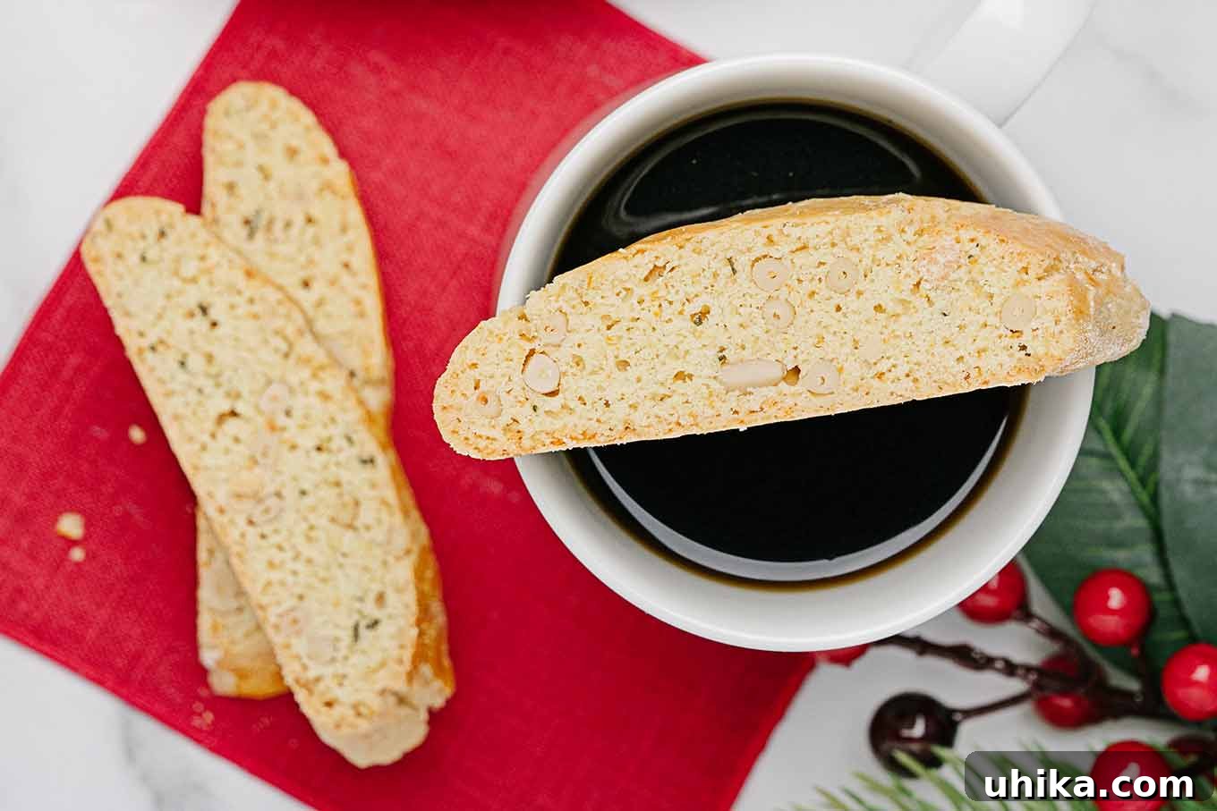 Zesty Butter Biscotti: A Double Treat 8 An overhead shot of orange rosemary biscotti delicately balanced on a coffee mug, with a red napkin underneath, and two more biscotti and a sprig of holly decoratively placed to the side.