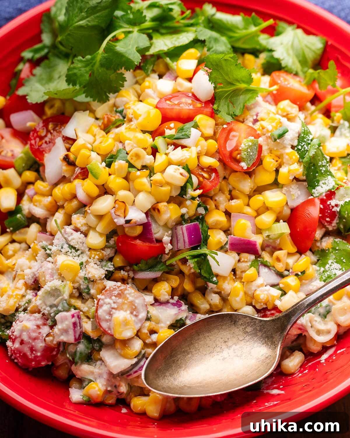 Esquites Corn Salad 2 A vibrant red bowl filled with Mexican Street Corn Salad, garnished with fresh cilantro and a spoon, ready to be served.