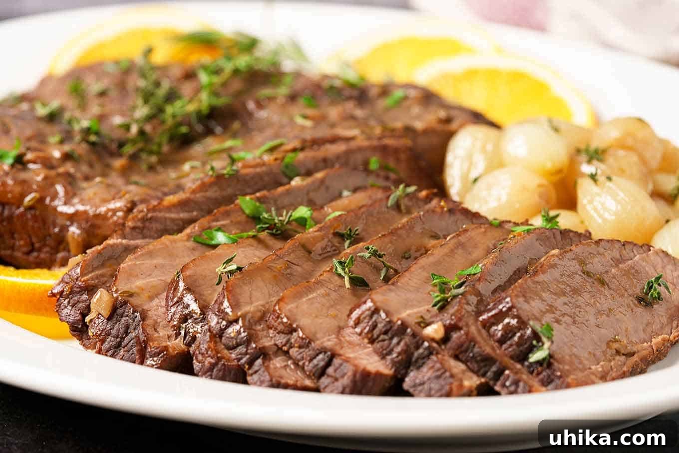 Melt-in-Your-Mouth Red Wine Brisket 3 A close-up view of perfectly sliced red wine braised beef brisket arranged on a platter, adorned with sweet pearl onions and a vibrant sprinkle of fresh parsley for an inviting garnish.