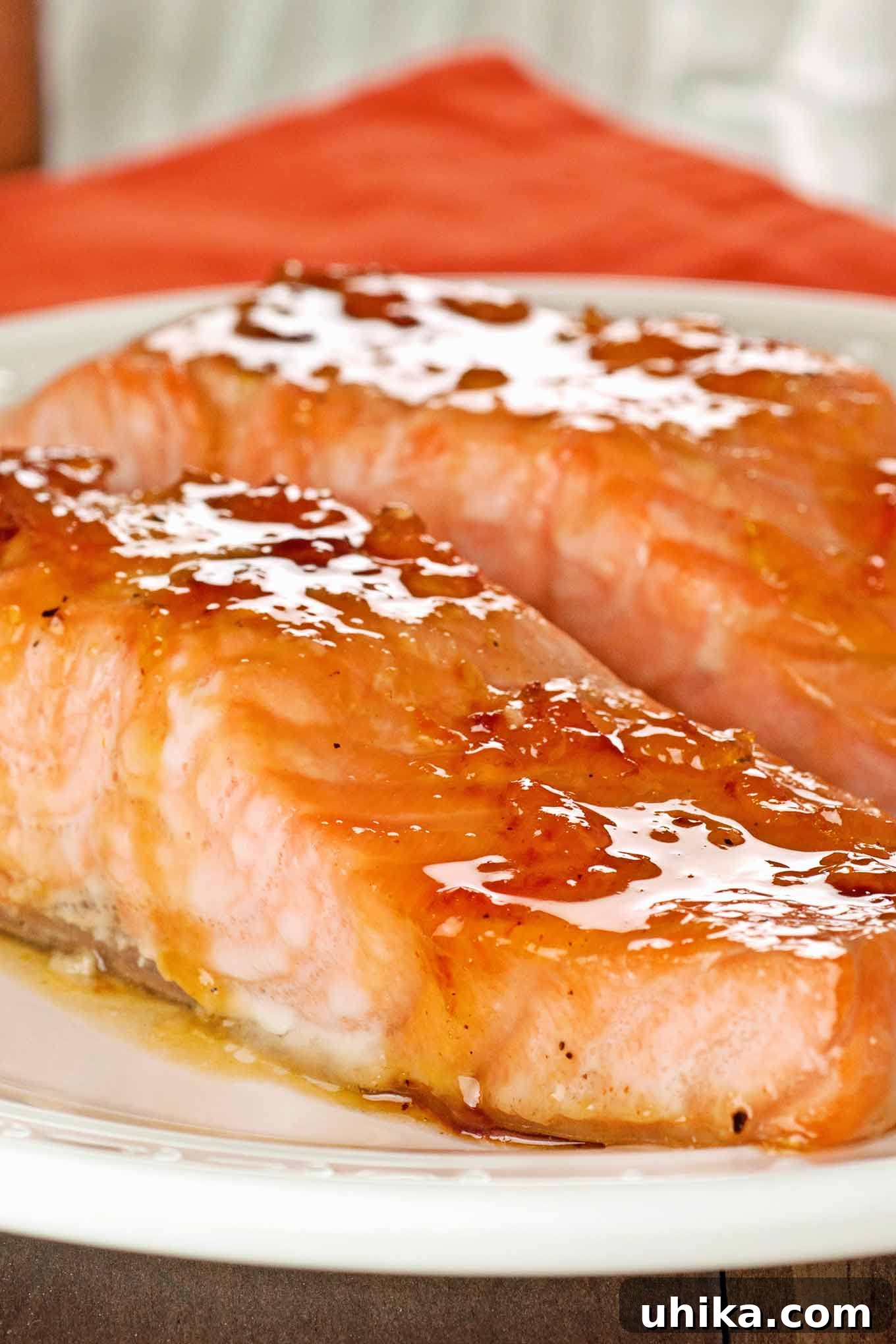 Sun-Kissed Bourbon Glazed Salmon 2 A white serving plate with two oven-roasted salmon fillets topped with a glistening orange marmalade and bourbon glaze, garnished with fresh herbs.
