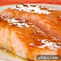 A white serving plate with two oven-roasted salmon fillets topped with orange marmalade and bourbon glaze.