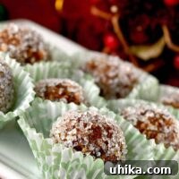 Homemade sugar plums rolled in coarse sugar, arranged holiday paper candy cups, Christmas decor in the background.
