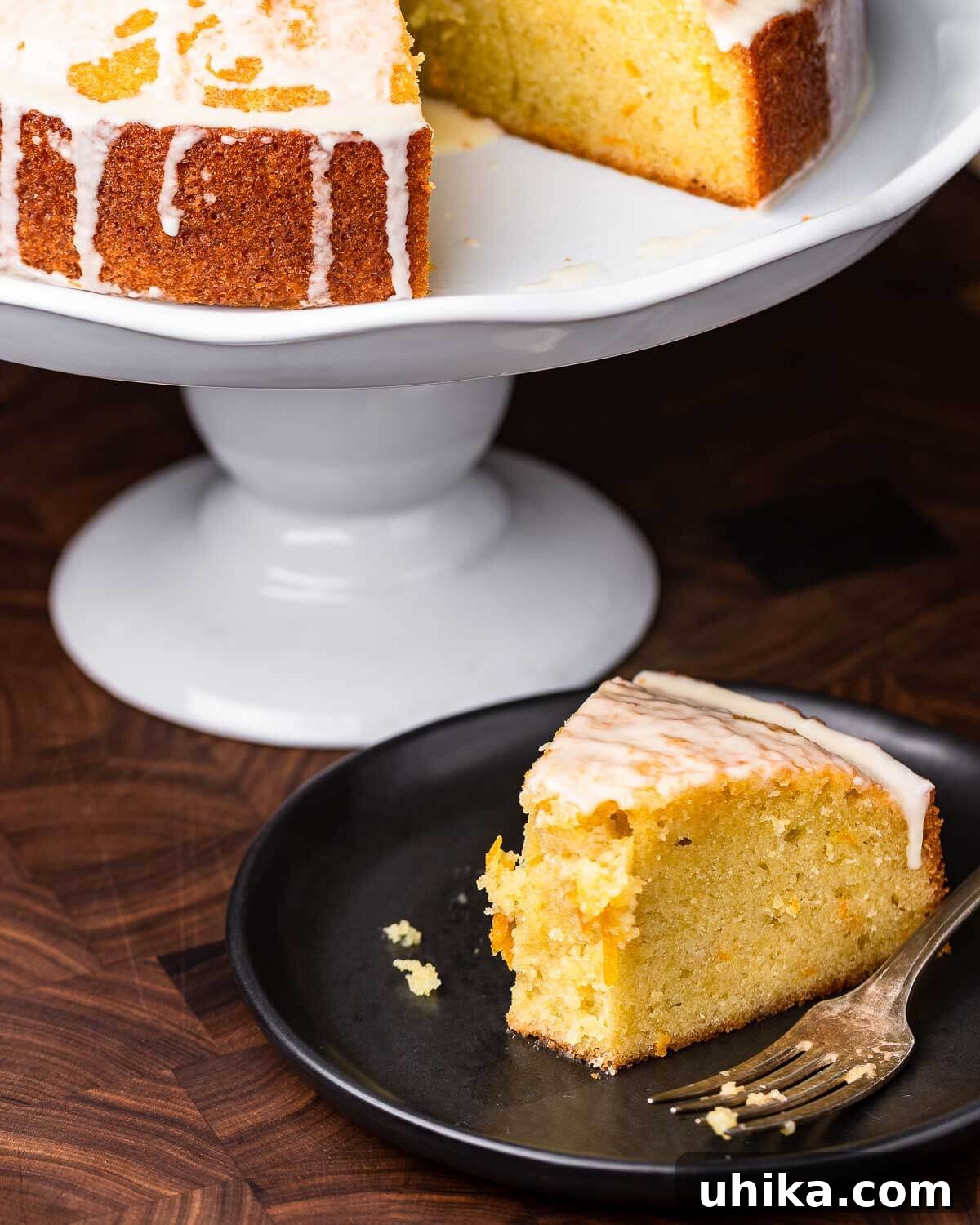 Cut piece of orange olive cake on black plate with cake stand in background.