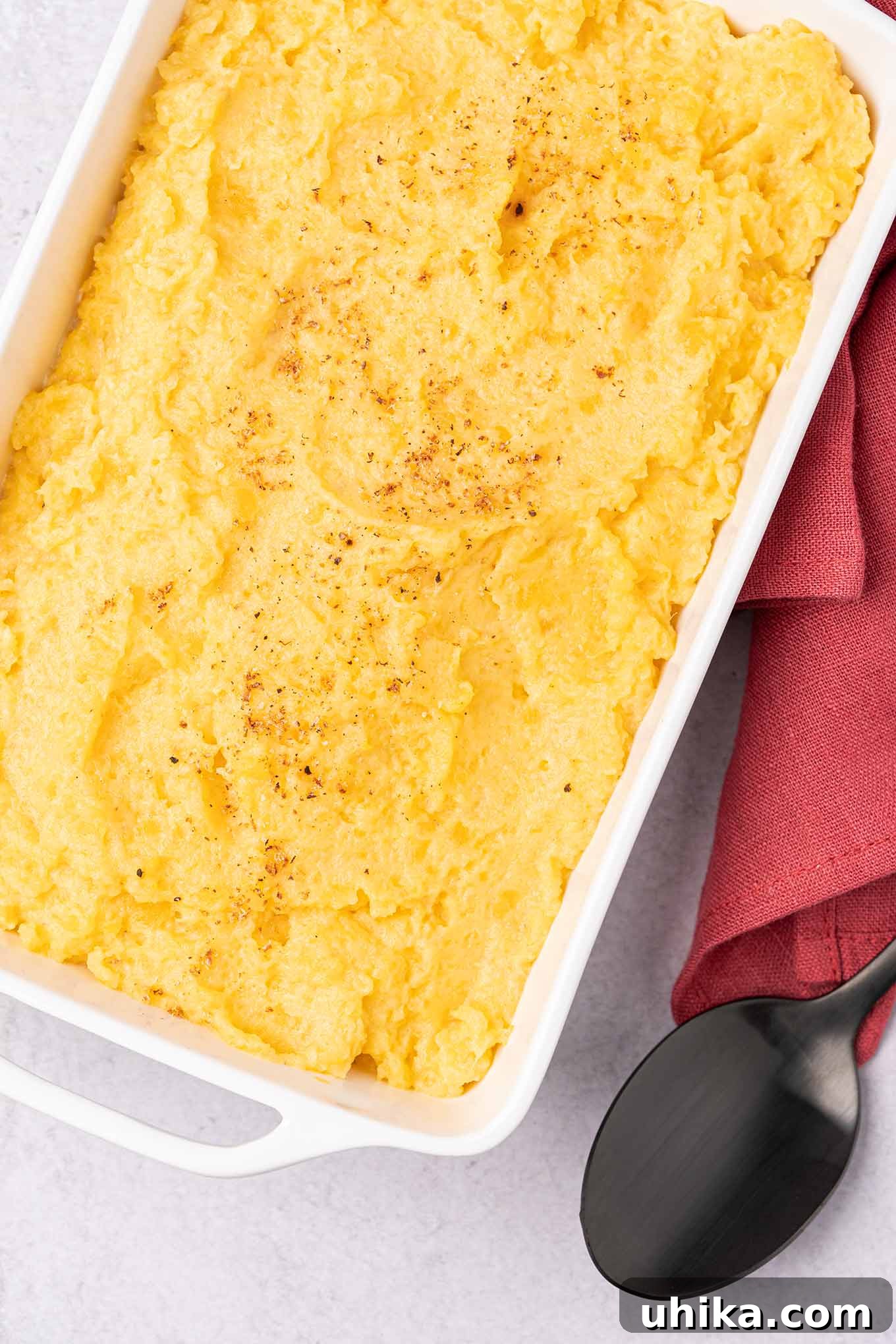 Velvety Rutabaga Mash 2 A white, oblong casserole dish of creamy mashed rutabagas sprinkled with nutmeg, a serving spoon and linen napkin on the side.