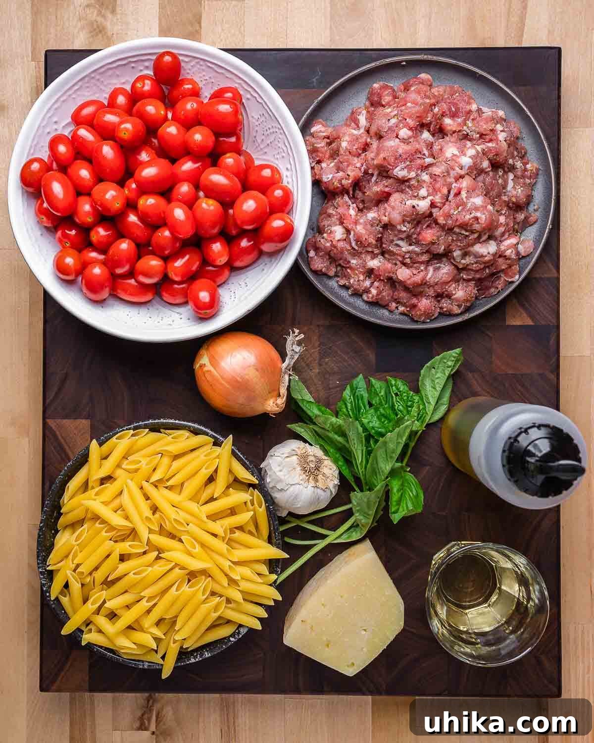 A vibrant flat lay of all ingredients for sausage cherry tomato pasta: penne, bulk Italian sausage, cherry tomatoes, onion, garlic, basil, olive oil, white wine, and Pecorino Romano cheese.