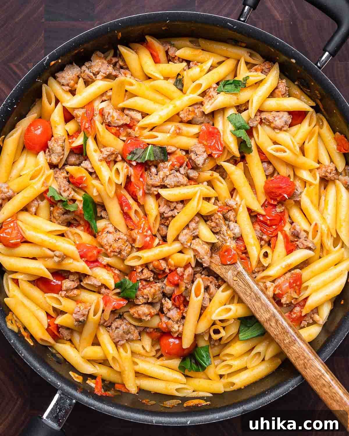 Overhead shot of freshly cooked sausage cherry tomato pasta in a black pan, ready to be served.