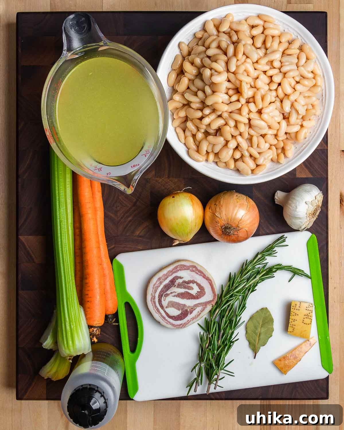 Rustic Tuscan White Bean Soup 3 A flat lay photograph showcasing all the ingredients required for Tuscan white bean soup, including cannellini beans, celery, carrots, onion, garlic, olive oil, pancetta, rosemary, and Parmigiano rinds.