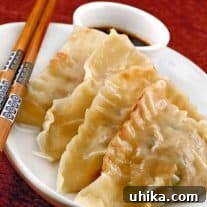 Savory Pork and Shrimp Parcels 3 Steamed shrimp and pork pot stickers arranged on a white plate with dipping sauce and a pair of decorative chopsticks.