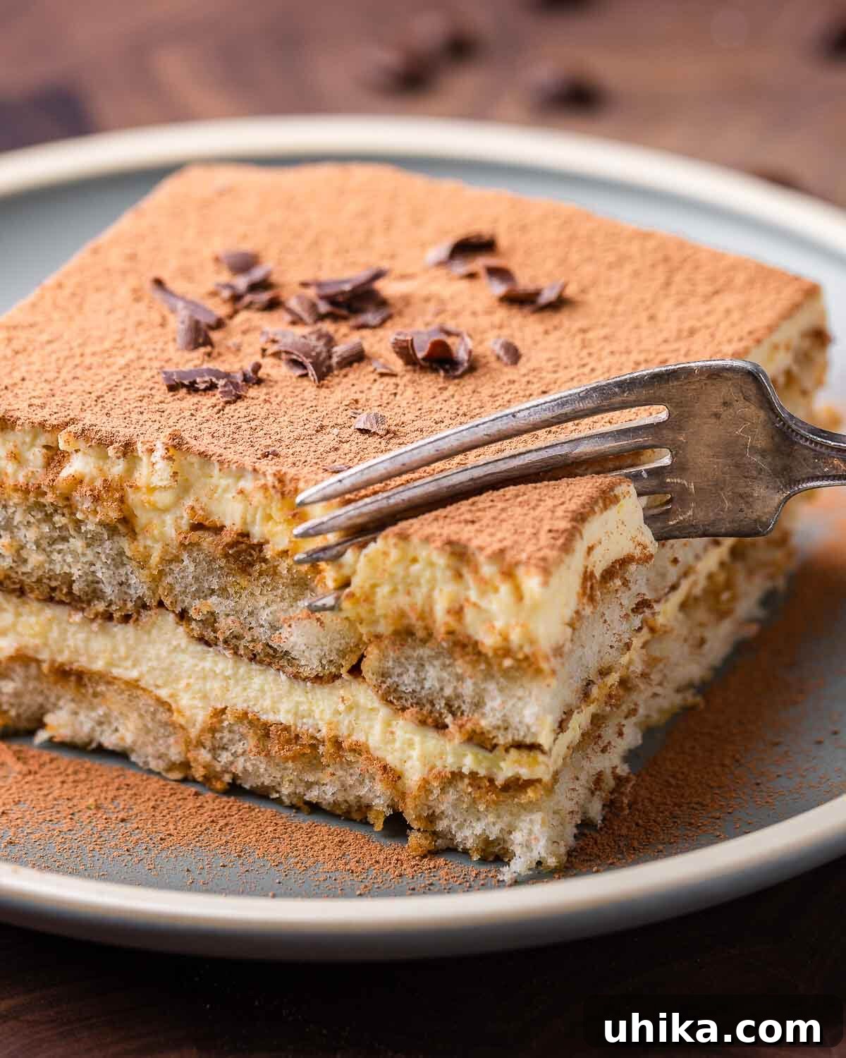 Tiramisu The Uplifting Dessert 2 A perfectly portioned slice of Tiramisu, showcasing its distinct layers, rests on a pristine white plate. A fork gently pierces the dessert, inviting a taste of its creamy goodness.