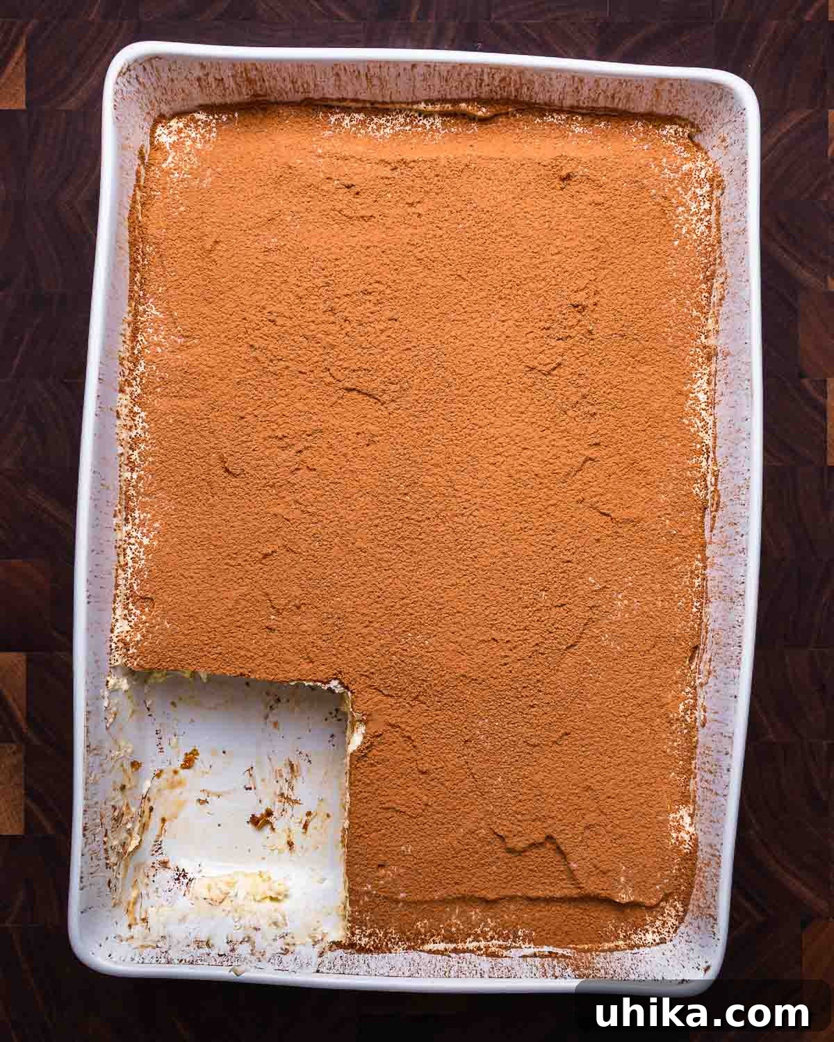 Tiramisu The Uplifting Dessert 8 A large rectangular baking dish filled with Tiramisu, from which a generous portion has been freshly cut, revealing its enticing layers of coffee-soaked ladyfingers and creamy mascarpone.