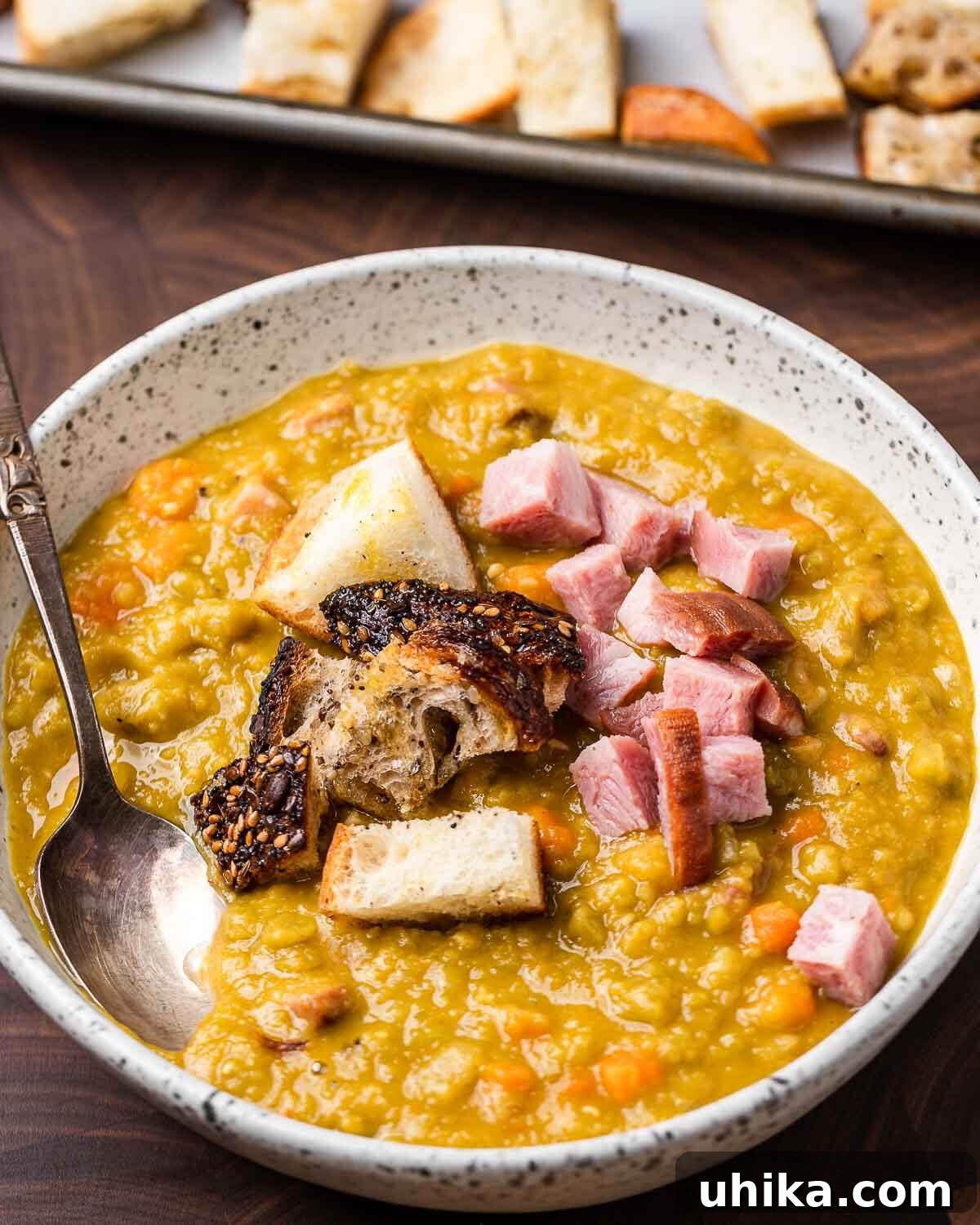 Hearty Smoked Ham and Split Pea Soup 7 White bowl of split pea soup and tray of croutons in background.
