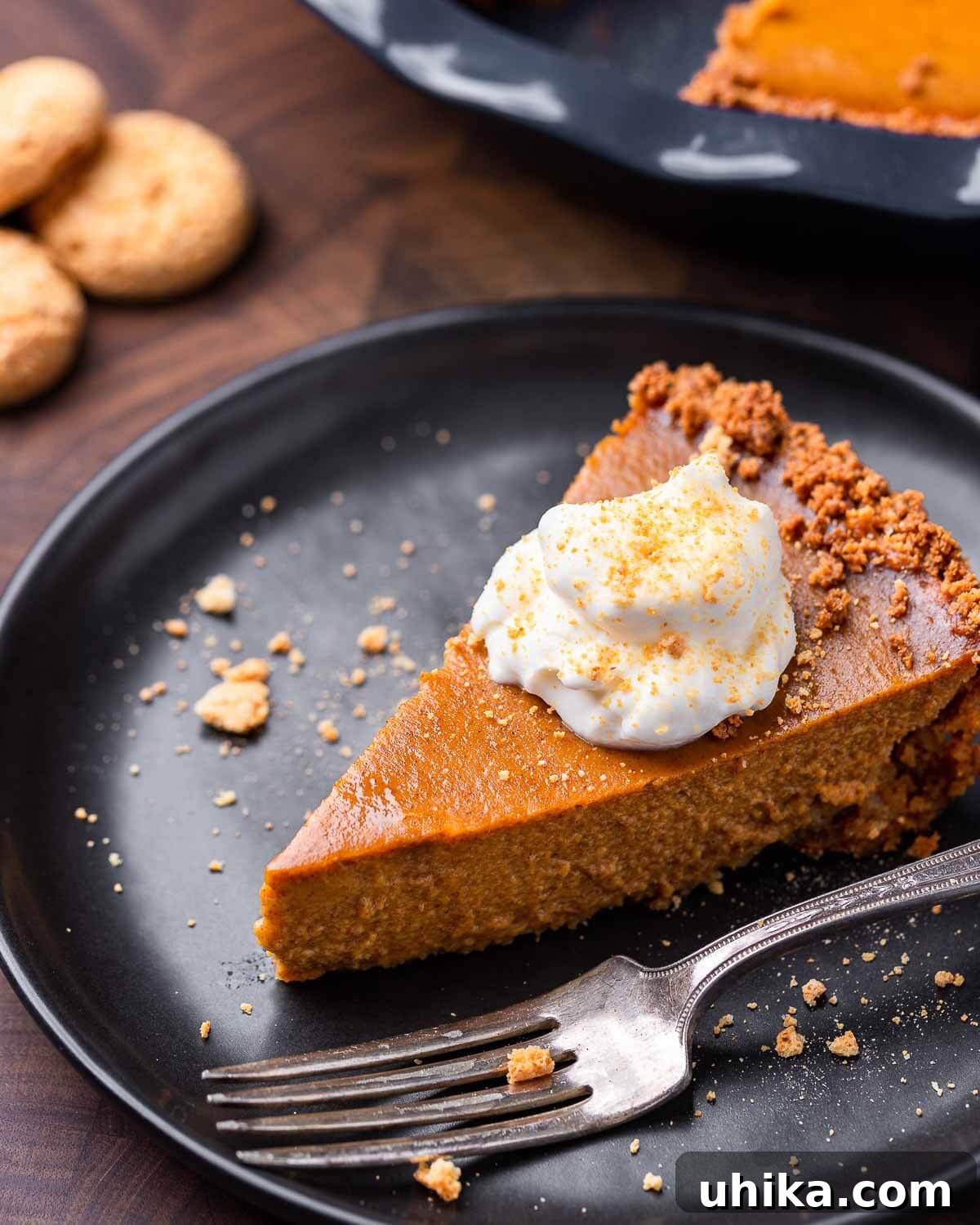 Amaretto Kissed Pumpkin Pie 8 A beautiful slice of pumpkin pie topped with a generous dollop of Amaretto whipped cream and sprinkled with crumbled amaretti cookies, served on a black plate.