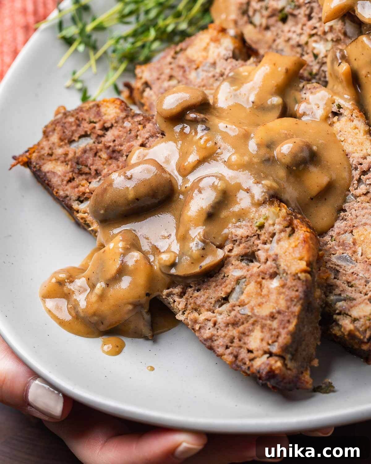 Ultimate Comfort Meatloaf with Rich Gravy 2 Hands holding platter of meatloaf with mushroom brown gravy, showcasing a generous portion of this comforting dish.