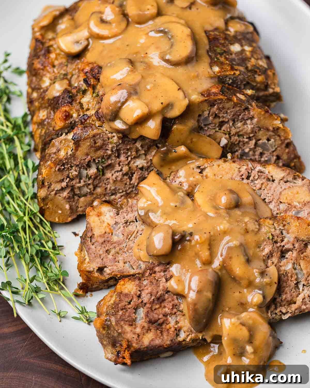 Ultimate Comfort Meatloaf with Rich Gravy 6 Slices of meatloaf with mushroom brown gravy on a white platter, ready to be served.