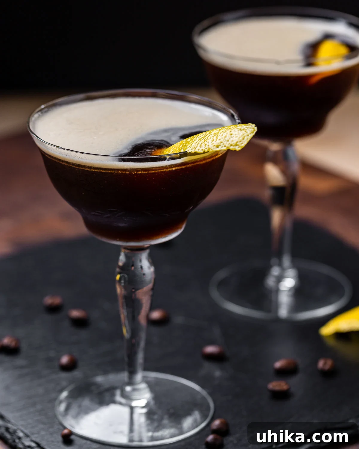Velvet Nightcap 5 Two perfectly crafted espresso martinis on a sleek black slate tile, garnished with lemon peels.