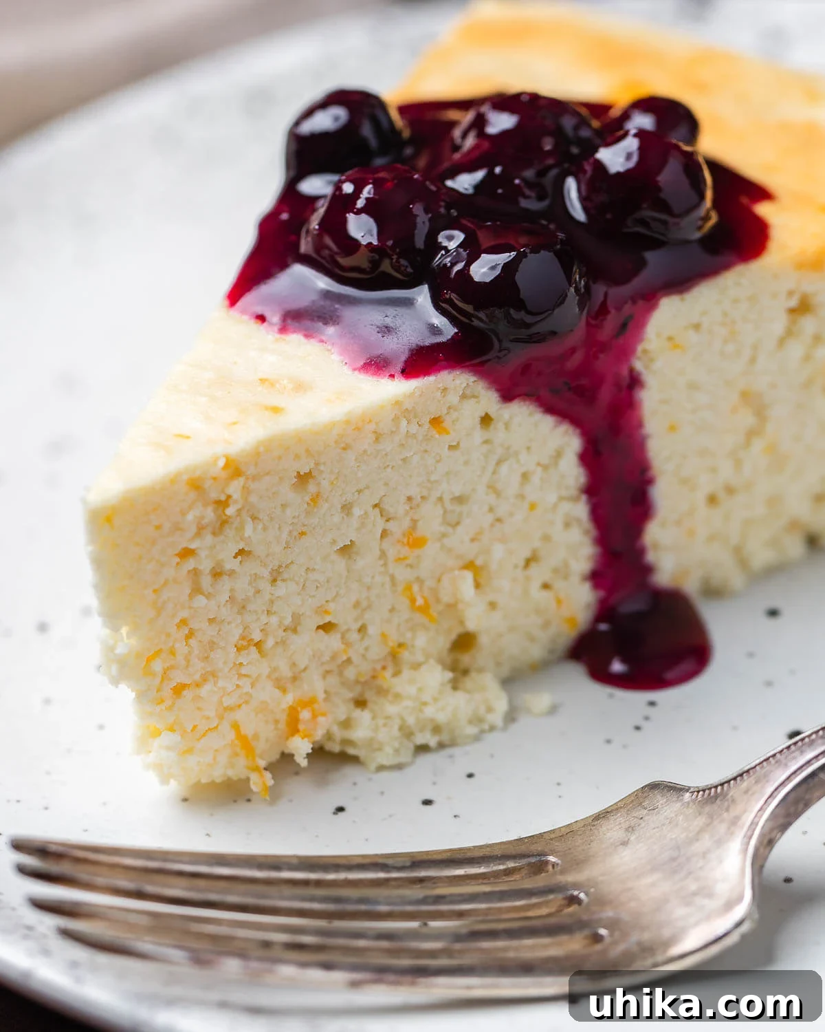 Nonna's Italian Cheesecake 2 A stunning slice of Italian cheesecake, generously drizzled with a bright lemon blueberry sauce, presented on a pristine white plate. The creamy texture of the cheesecake is visible beneath the vibrant fruit topping.