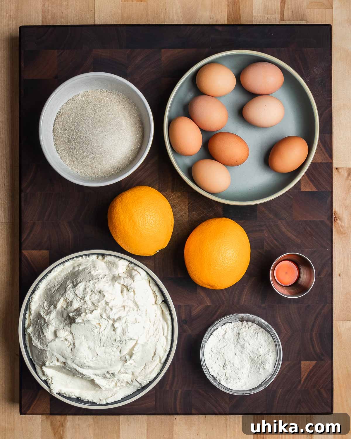 Nonna's Italian Cheesecake 3 A carefully arranged collection of essential ingredients for Italian cheesecake: granulated sugar, fresh eggs, whole oranges, fragrant vanilla extract, creamy ricotta cheese, and sifted flour, awaiting their transformation.