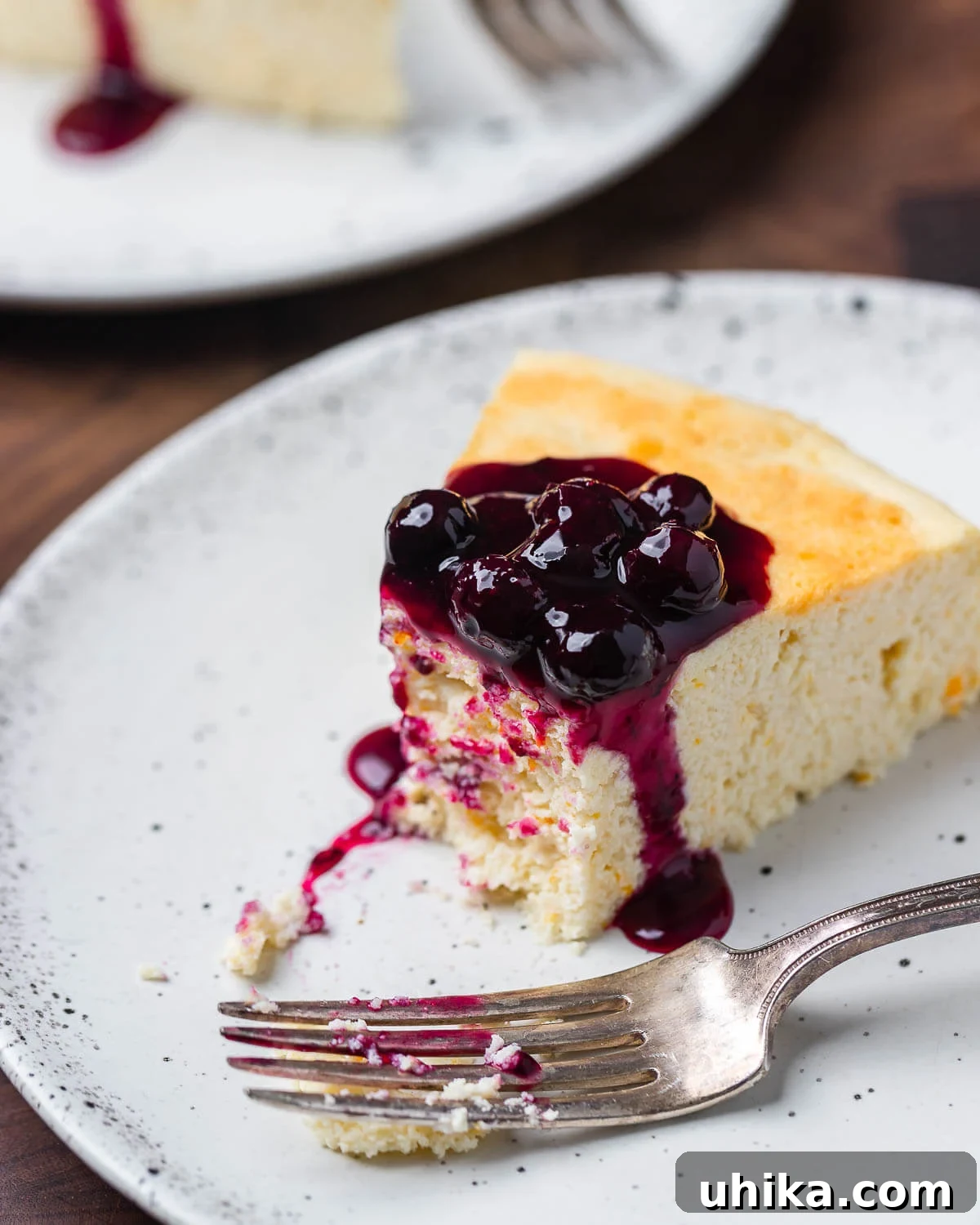 Nonna's Italian Cheesecake 8 A perfectly sliced Italian cheesecake, with a creamy interior and golden top, resting on a white plate. A gentle bite has been taken, revealing the airy texture within, and a hint of blueberry sauce adds a touch of color.