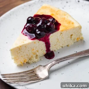 Italian cheesecake recipe featured image: a top-down view of a whole cheesecake with a slice removed, showing its creamy texture, and a small bowl of blueberry sauce nearby.