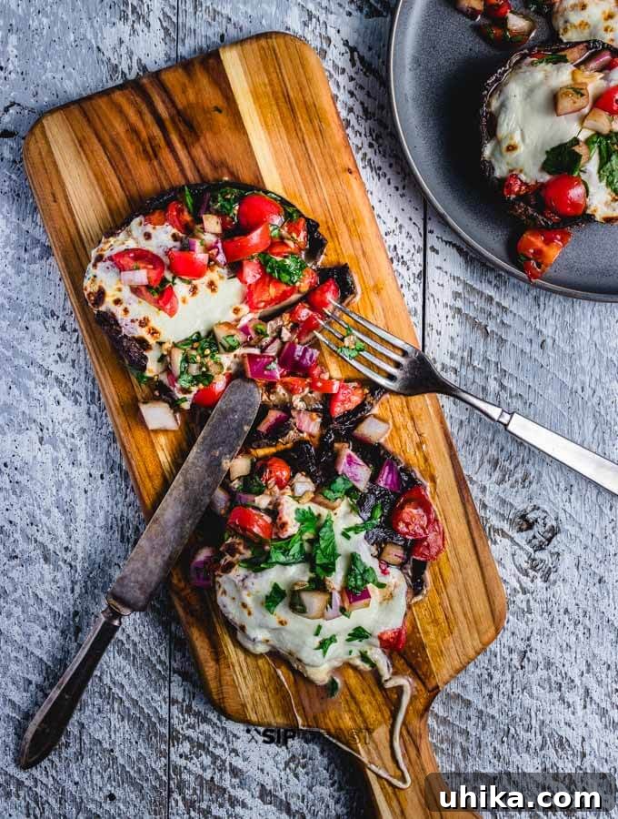 Delicious baked stuffed portobello mushrooms with bruschetta and mozzarella. Final plated dish of baked portobello mushrooms, stuffed with bruschetta and topped with melted mozzarella and fresh parsley.
