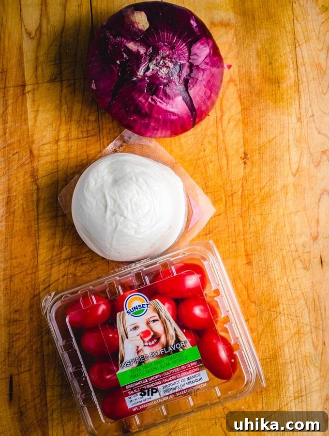 Key ingredients for our Baked Portobello Mushrooms recipe. Fresh cherry tomatoes, a red onion, and fresh mozzarella cheese slices on a wooden board for bruschetta preparation.