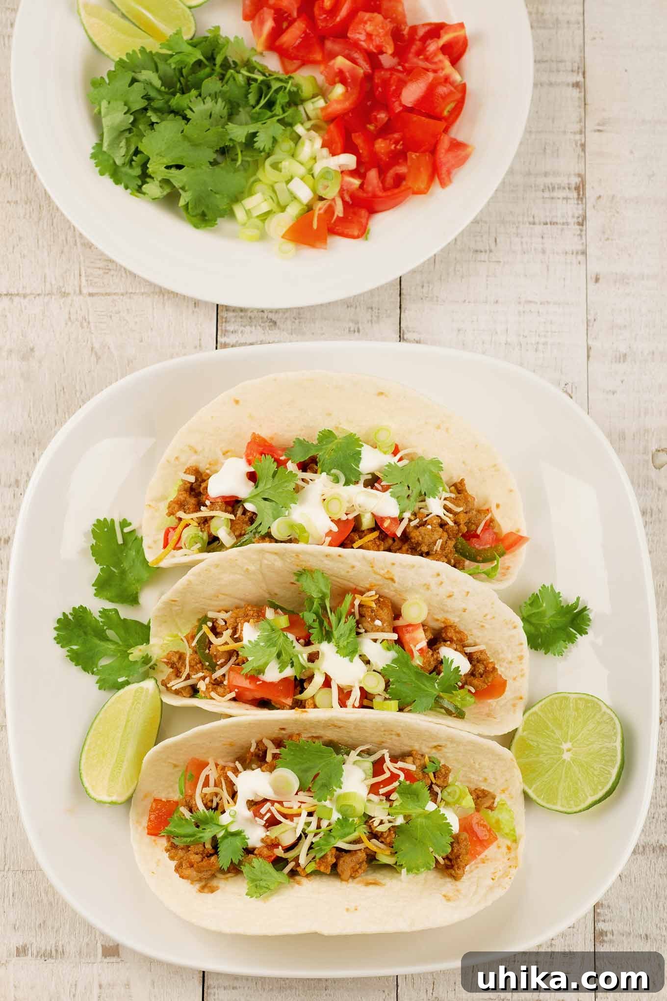 Zesty Turkey Tacos 3 An overhead view of a plate of ground turkey tacos on a light wooden surface, next to a plate of toppings in the background, ready for serving.