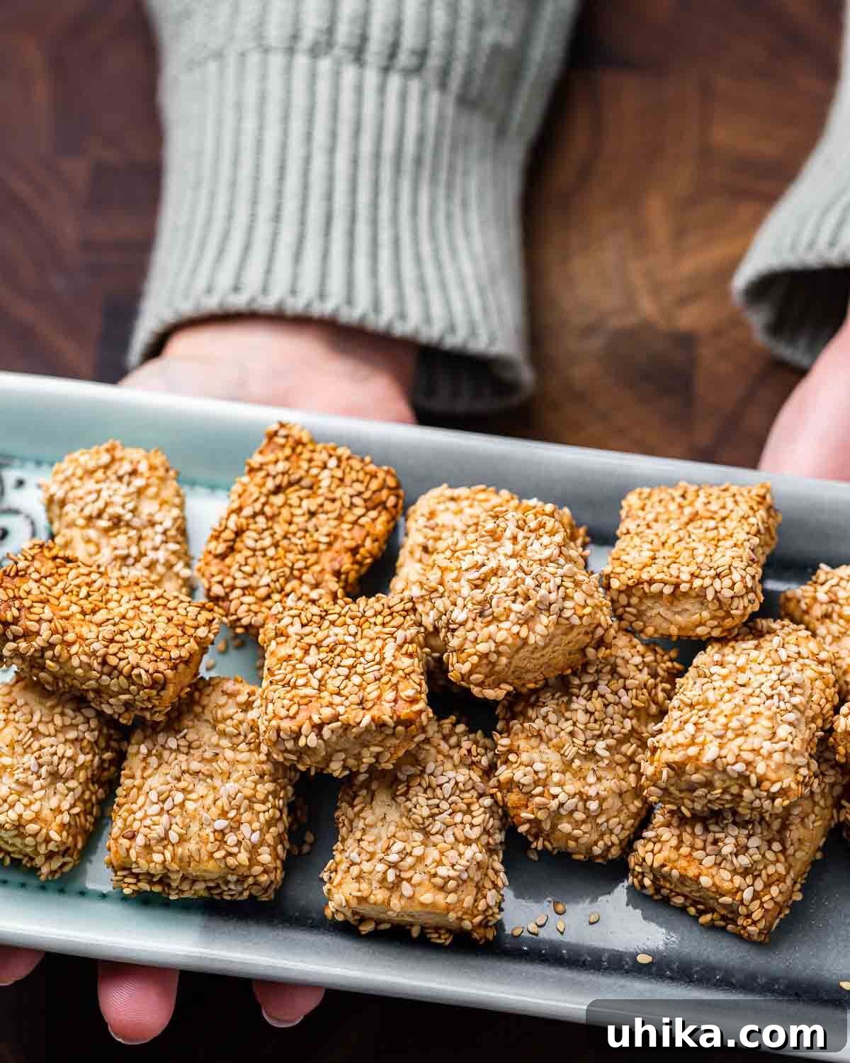Crispy Sesame Delights 8 Hands presenting a platter of golden-brown Reginelle cookies, beautifully coated in sesame seeds.