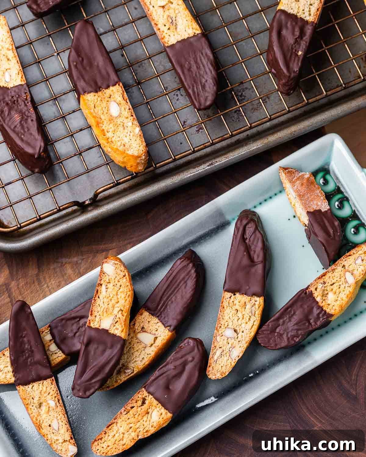 Twice-Baked Almond Delights 9 Almond biscotti dipped in chocolate on blue plate along with more biscotti on wire rack in the background.