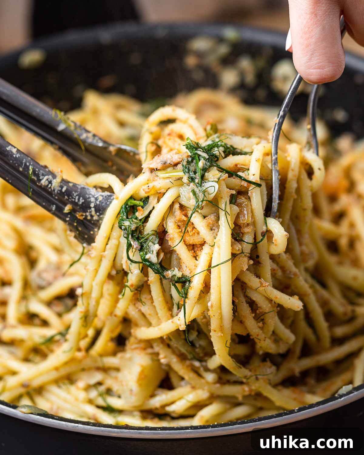 Sicilian Sardine Pasta 2 Hands tossing freshly prepared Pasta con le Sarde in a large bowl.