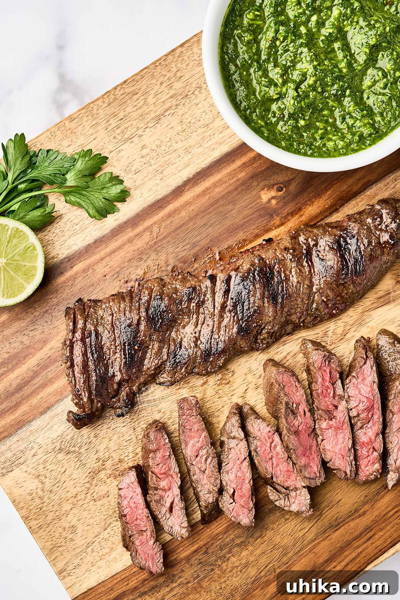 Sizzling Steak, Vibrant Chimichurri 5 Grilled skirt steak partially sliced on a wooden cutting board, ready to be topped with chimichurri sauce from the bowl beside it.