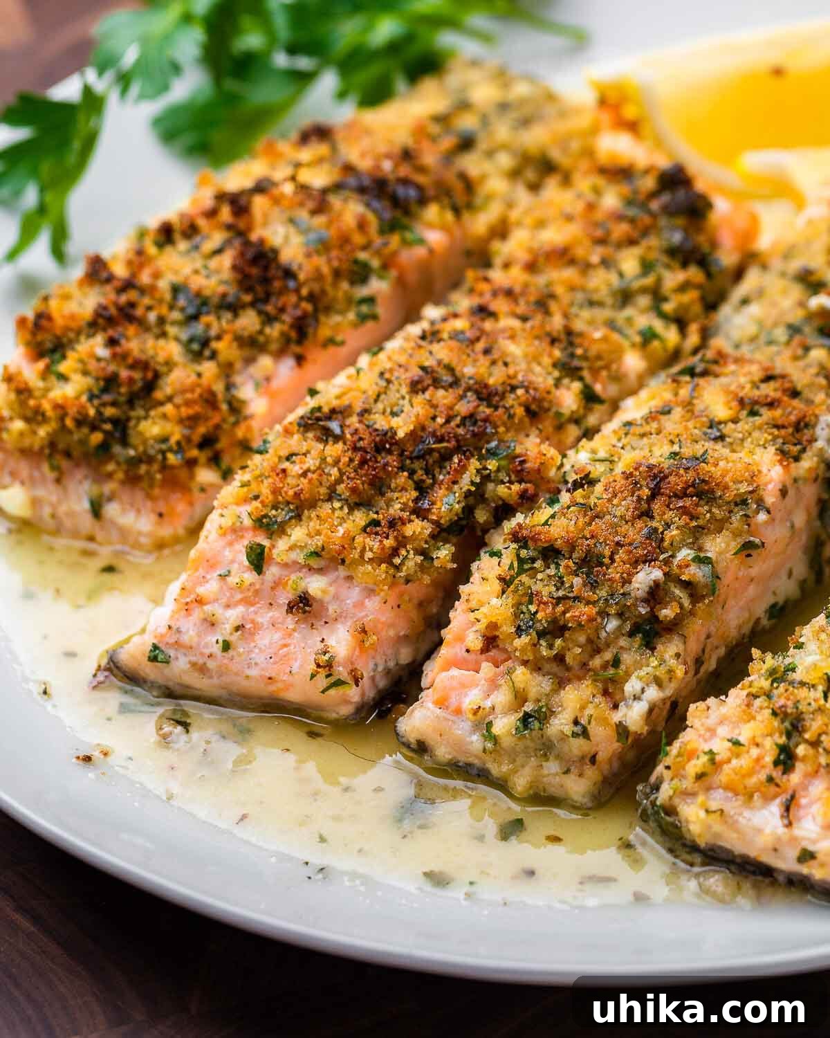Golden Oregano Crusted Salmon 2 Salmon oreganata in butter sauce on white plate, garnished with fresh parsley and lemon.