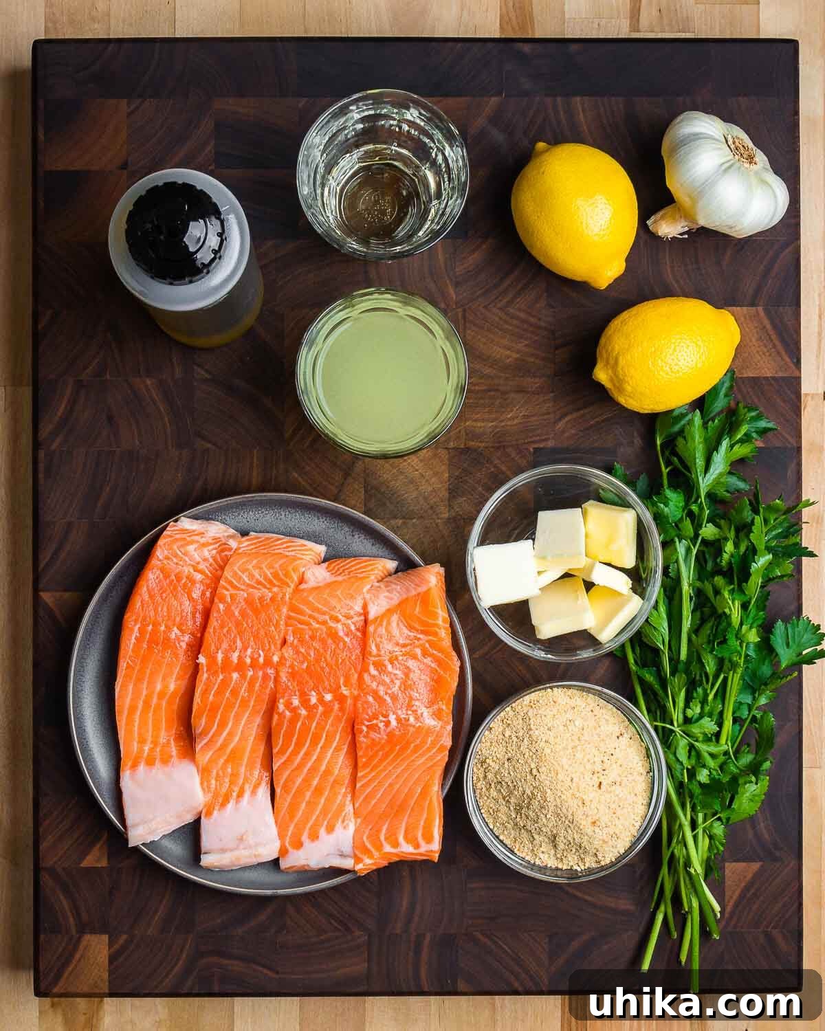 Golden Oregano Crusted Salmon 3 Fresh ingredients for Salmon Oreganata laid out: olive oil, white wine, chicken stock, lemons, garlic, salmon, butter, breadcrumbs, and parsley.