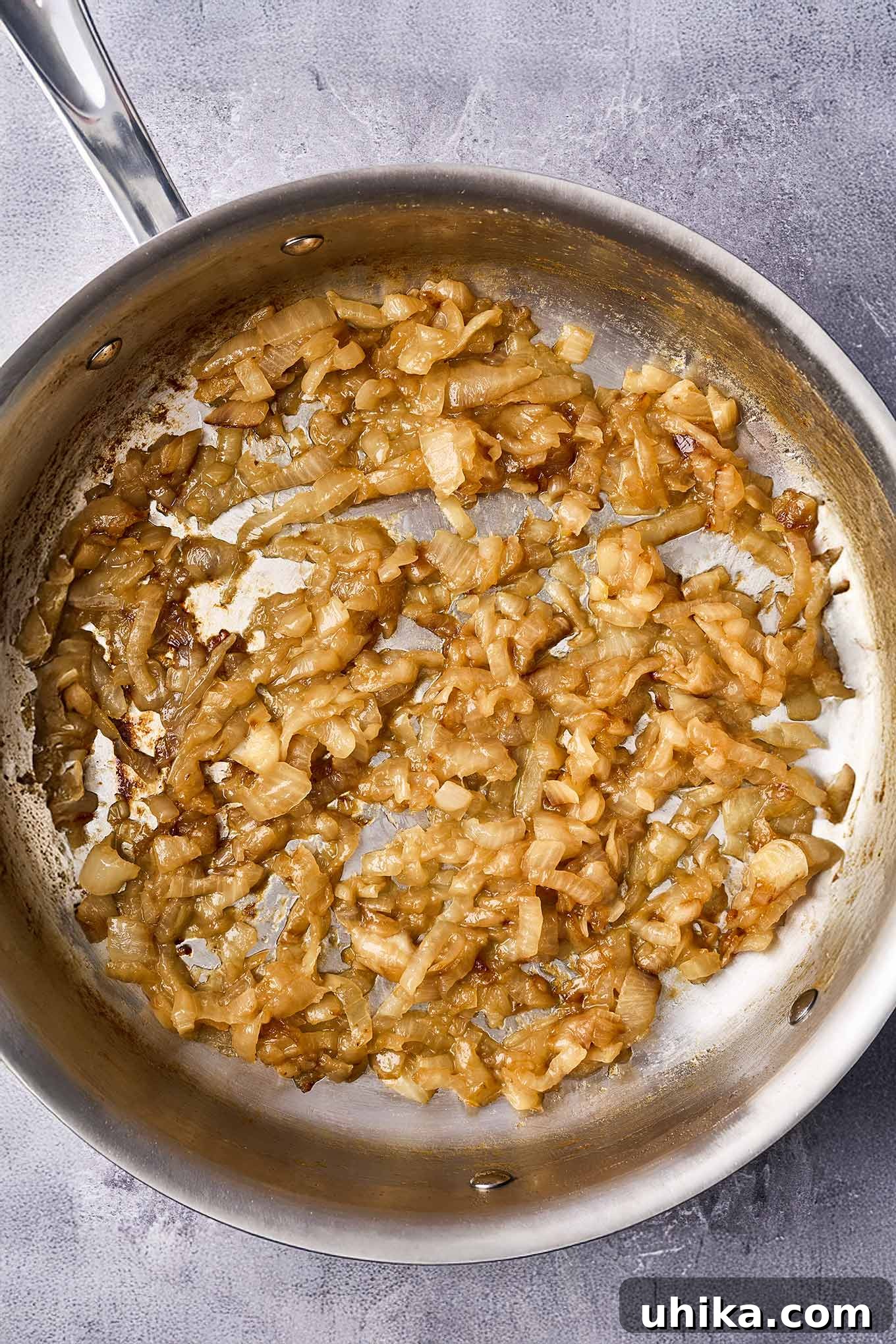 Caramelized onions in a stainless steel skillet, cooked to a beautifully golden-brown color with some texture remaining, ideal for topping dishes. This stage typically takes 35-40 minutes.