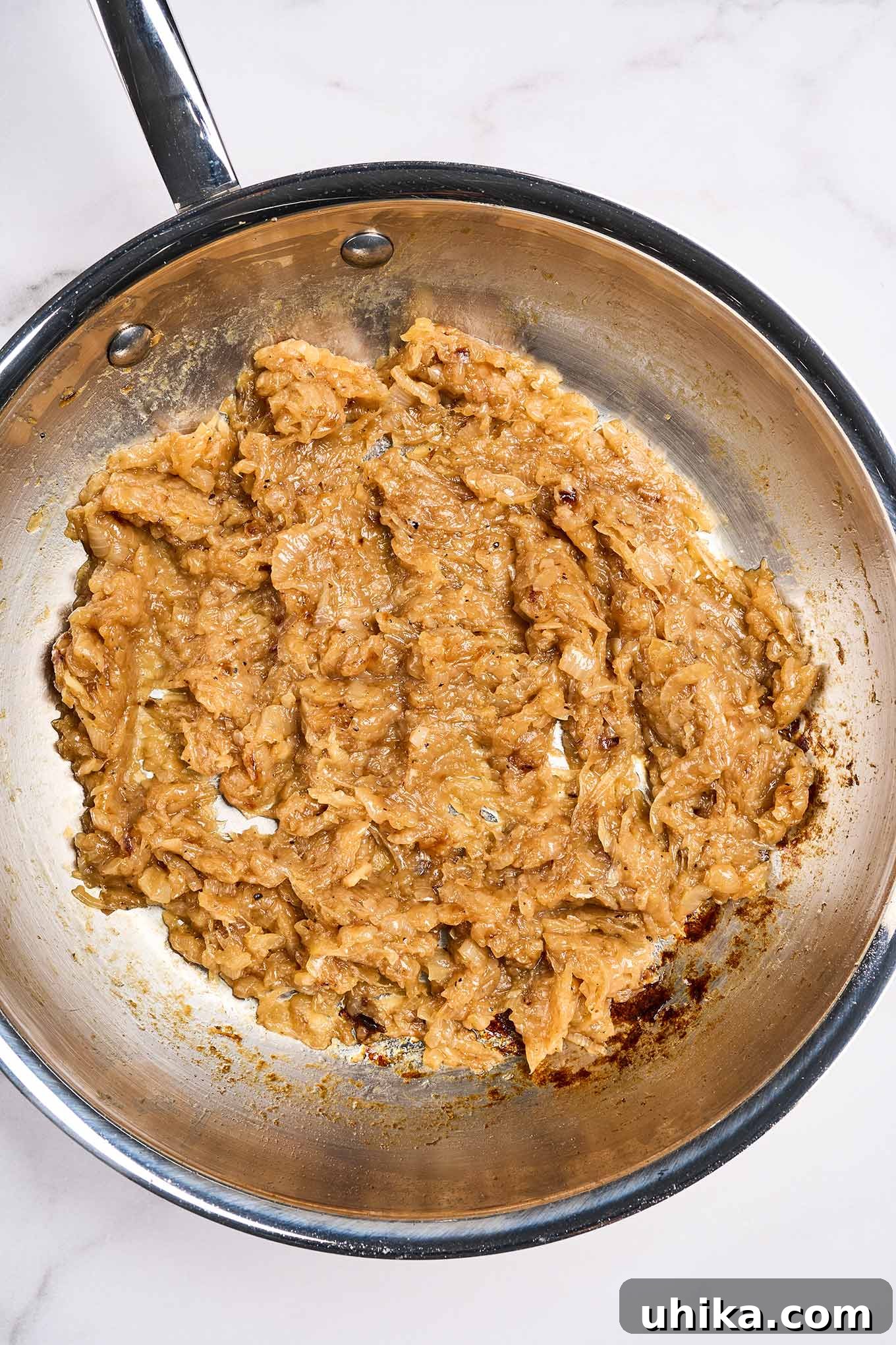 Fully caramelized onions in a stainless steel skillet, reduced to a rich, dark golden-brown, spreadable, jam-like consistency, perfect for soups or spreads. This deep caramelization takes 45-50 minutes.