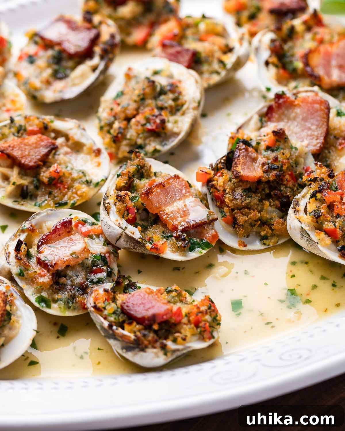 Baked Clams Royale 2 Clams casino arranged neatly on a pristine white platter, garnished with fresh herbs and lemon wedges, ready to be served.