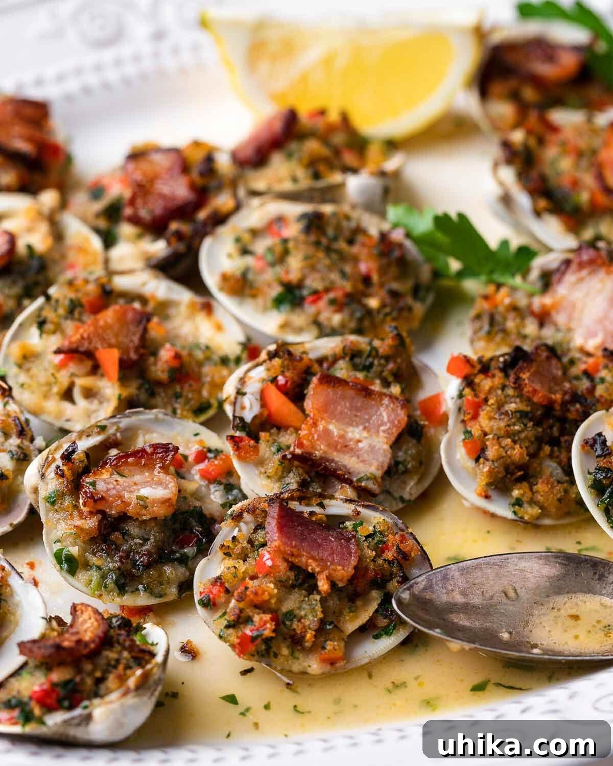 Baked Clams Royale 9 Clams casino glistening on a white plate, accompanied by bright yellow lemon wedges, ready to be enjoyed as a gourmet seafood appetizer.