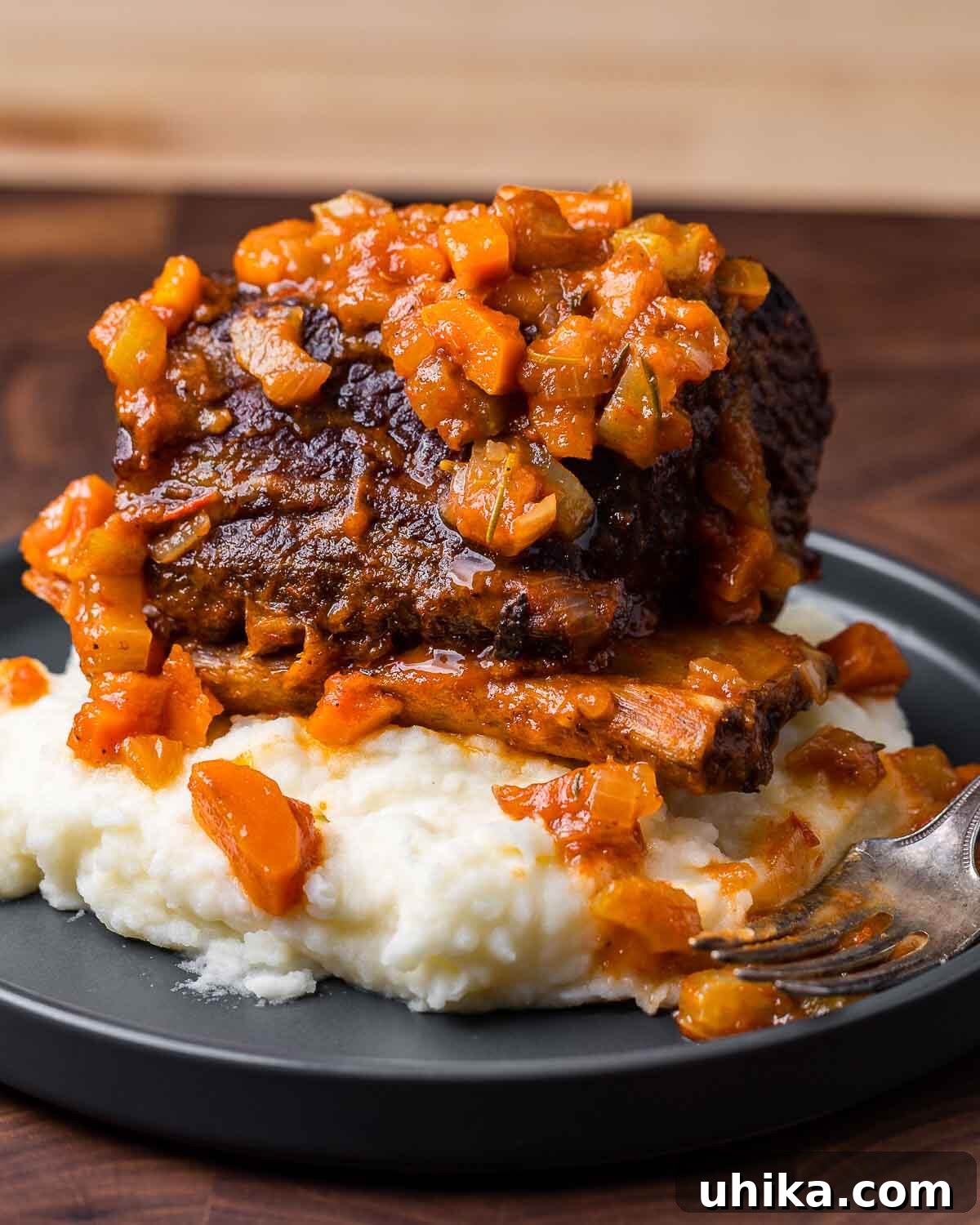 Fall-Off-The-Bone Short Ribs 2 A large, perfectly braised short rib rests atop a bed of creamy mashed potatoes in an elegant grey plate, promising a comforting and hearty meal.