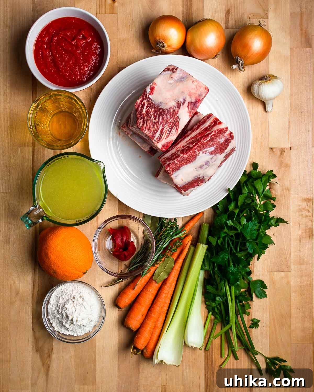 Fall-Off-The-Bone Short Ribs 3 An overhead shot showcasing the fresh ingredients for braised short ribs, including carrots, celery, onions, garlic, and herbs. An orange and parsley for the optional gremolata are also visible.