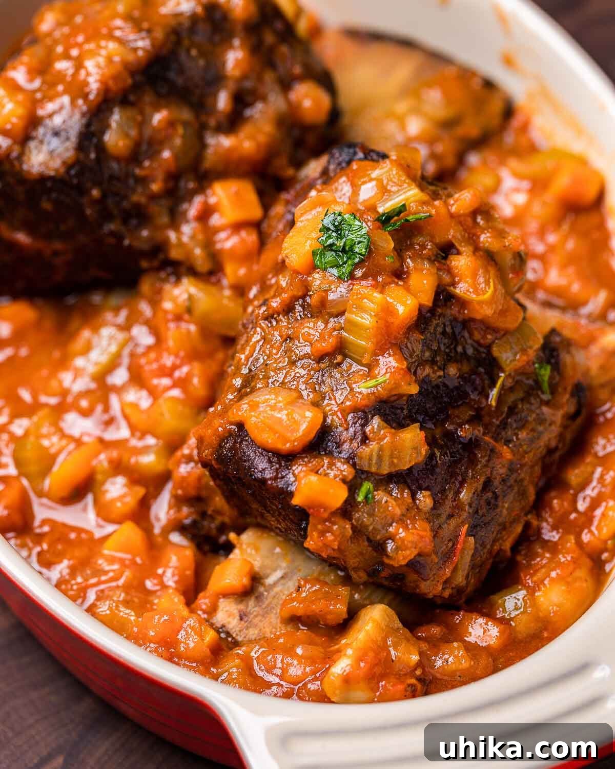 Fall-Off-The-Bone Short Ribs 6 Two succulent braised short ribs rest invitingly in a baking dish, submerged in their rich, savory sauce, ready to be served.