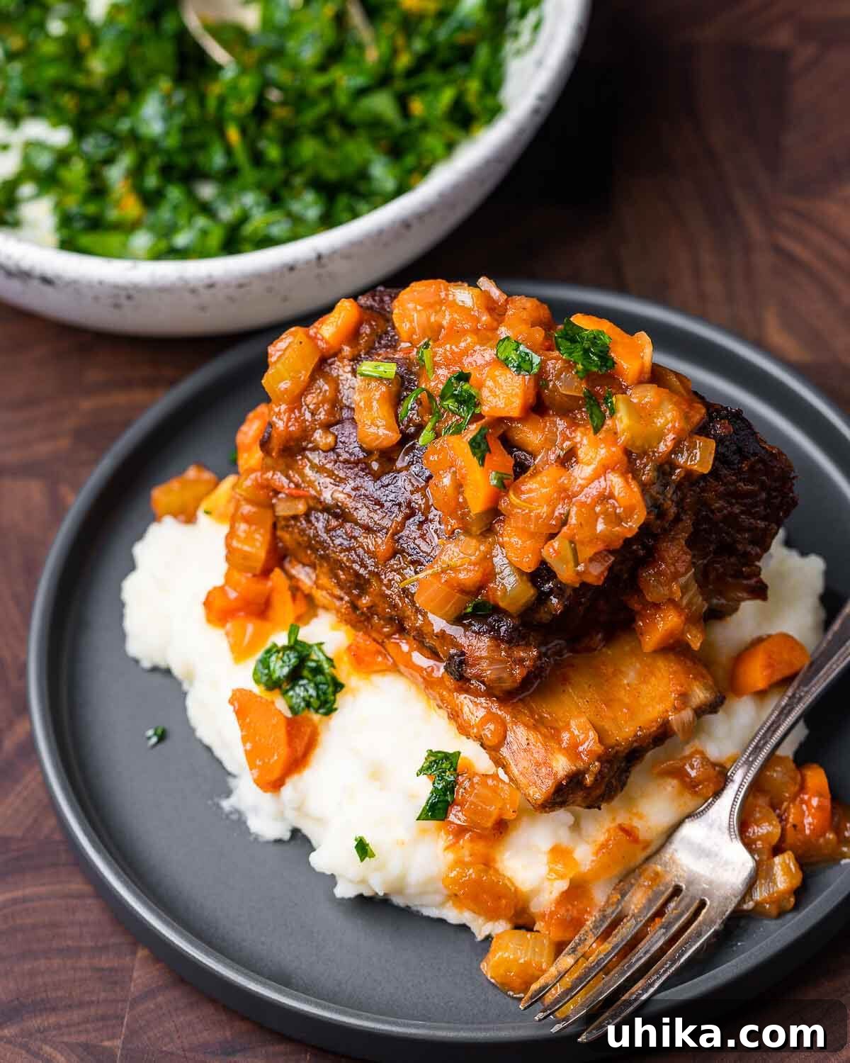 Fall-Off-The-Bone Short Ribs 8 A perfectly cooked braised short rib, glistening with its rich sauce, served over a bed of creamy mashed potatoes on a sophisticated grey plate, highlighting its comfort food appeal.
