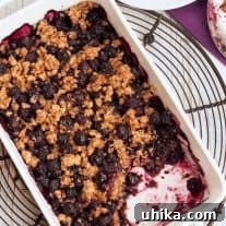 Blueberry Bliss with a Cornflake Crunch 3 Freshly baked blueberry crisp in a baking dish with a serving removed and placed on a plate to the side. Golden, crispy topping and bubbling, juicy blueberries are visible.