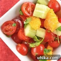 Close-up of a colorful Tomato, Orange, and Cucumber Salad in a white bowl.