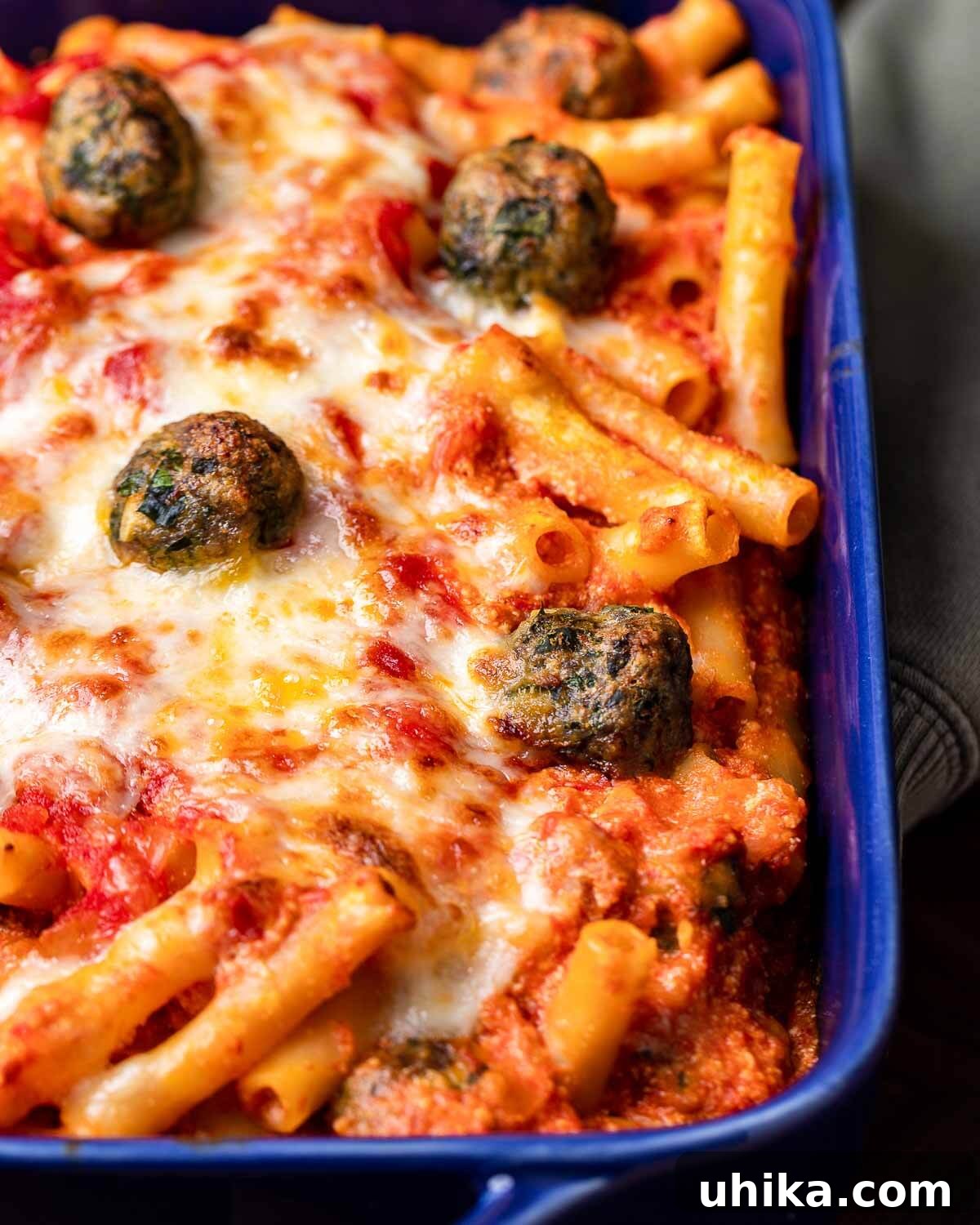 Cheesy Meatball Ziti Bake 2 Hands holding blue baking dish with baked ziti and tiny meatballs, showcasing the golden, bubbly top.