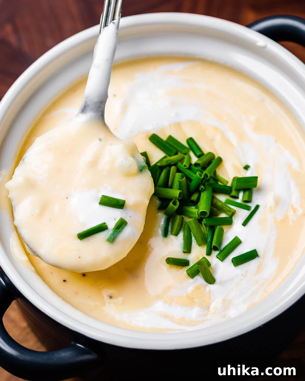 Hearty Loaded Potato Soup 2 Spoon holding creamy baked potato soup over blue bowl. A perfect serving of loaded baked potato soup ready to eat.