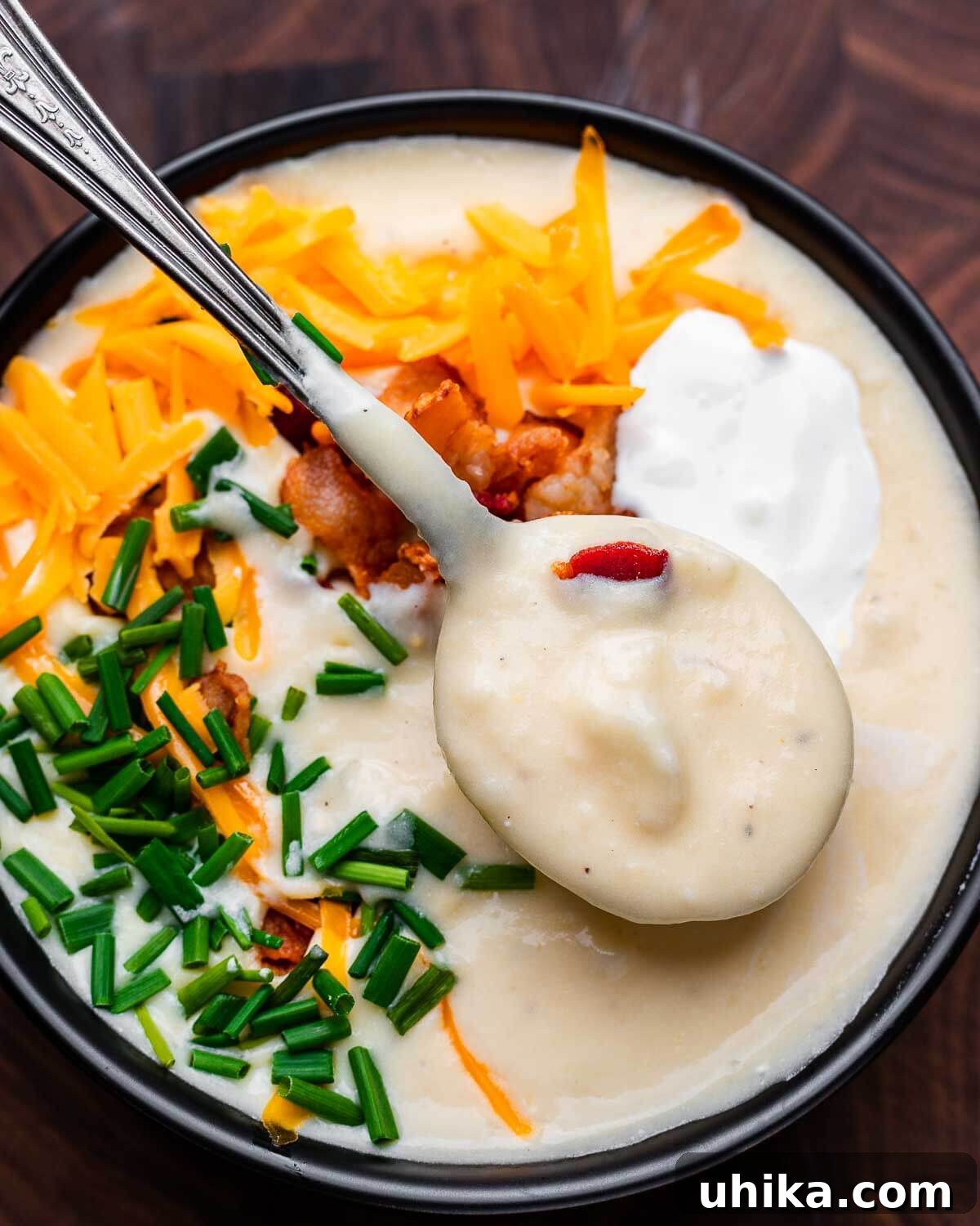Hearty Loaded Potato Soup 9 Black bowl of loaded baked potato soup, garnished with chives, bacon, and sour cream.