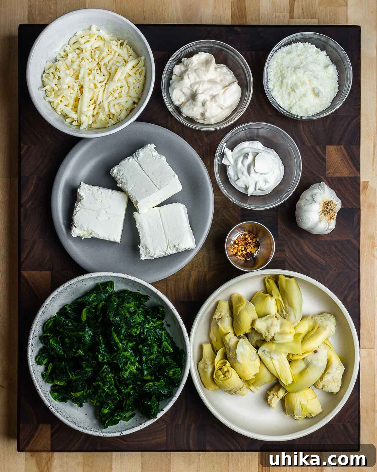 Irresistible Spinach Artichoke Dip 3 A vibrant flat lay shot displaying all the fresh ingredients for spinach artichoke dip: mozzarella, mayonnaise, Pecorino Romano, cream cheese, sour cream, hot red pepper flakes, garlic, spinach, and artichoke hearts, neatly arranged.