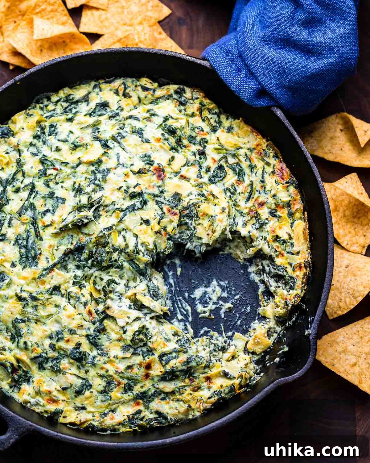 Irresistible Spinach Artichoke Dip 7 Overhead shot of a rustic cast iron pan filled with hot, bubbling spinach artichoke dip, surrounded by crispy tortilla chips for dipping.