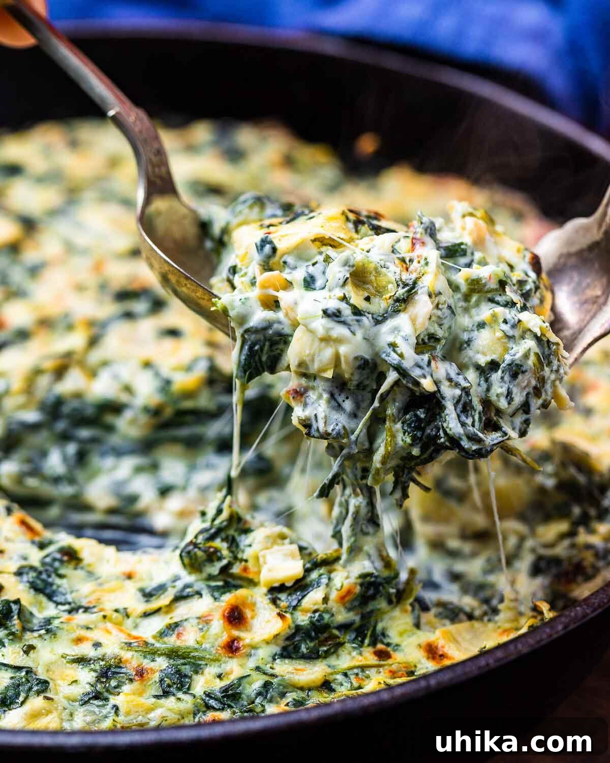Irresistible Spinach Artichoke Dip 8 Two forks lifting hot, stringy, and incredibly creamy spinach artichoke dip directly from a rustic cast iron pan, highlighting its appealing texture.